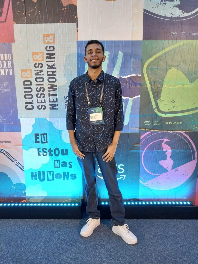 Jovem em pé, em frente ao backdrop do evento da AWS Summit