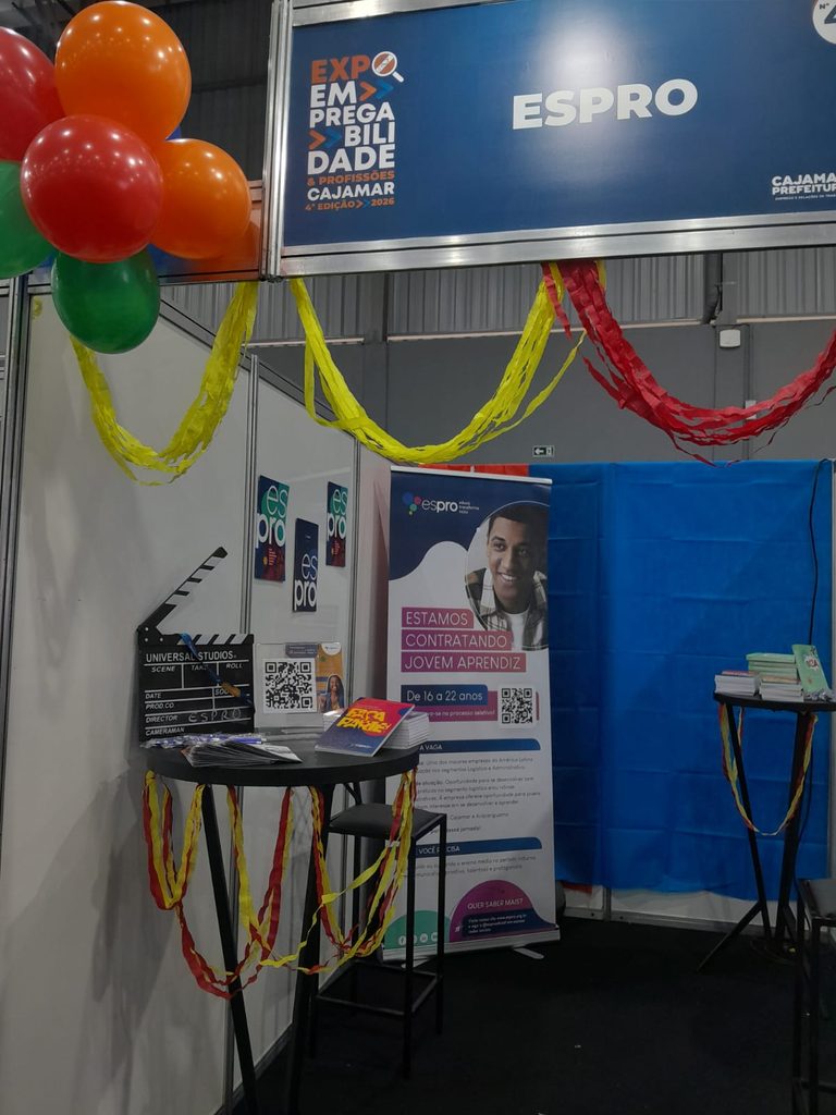 Estande do Espro na Expo Empregabilidade de Cajamar, com banner "Estamos Contratando Jovem Aprendiz", claquete de cinema personalizada e decoração em vermelho, laranja e verde.